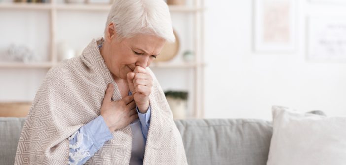 Sick senior woman covered in blanket and coughing